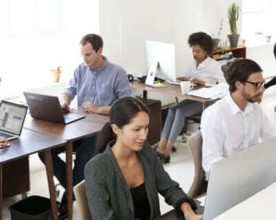 Two male and two female employees sitting at their desks in a bright office working on their Mac desktop computers